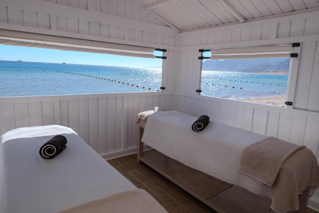 Mierīga spa telpa ar divām masāžas galdiem, skatoties uz jūru un saulainu ainavu. Logi ļauj baudīt dabu un relaksāciju.