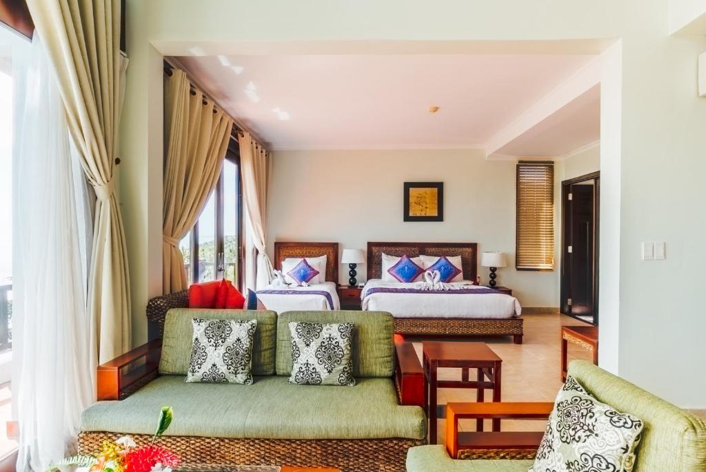 Elegantā viesnīcas numura interjers ar divām gultām, mīkstu dīvānu un plašiem logiem, kas nodrošina labu apgaismojumu. Gaismas toņi un moderns dizains rada relaksējošu atmosfēru.