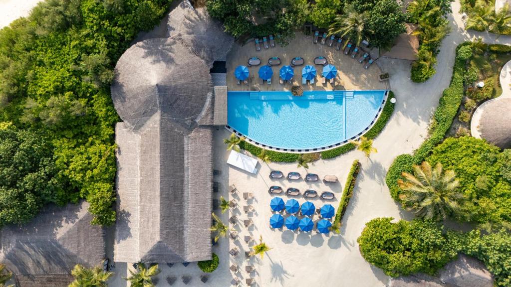 Viegla gaisa skats uz modernu viesnīcu ar baseinu un sauļošanās krēsliem, ko ieskauj zaļi koki un dārzi. Baseins ir izveidots ar zilu ūdeni un apveltīts ar sauļošanās lietussargiem.