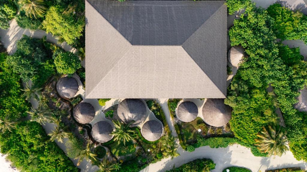 Apskatāma ainava ar jumtu un apaļām būdām, kas ieskautas zaļā veģetācijā. Šī ainava rada mierīgu un relaksējošu atmosfēru.