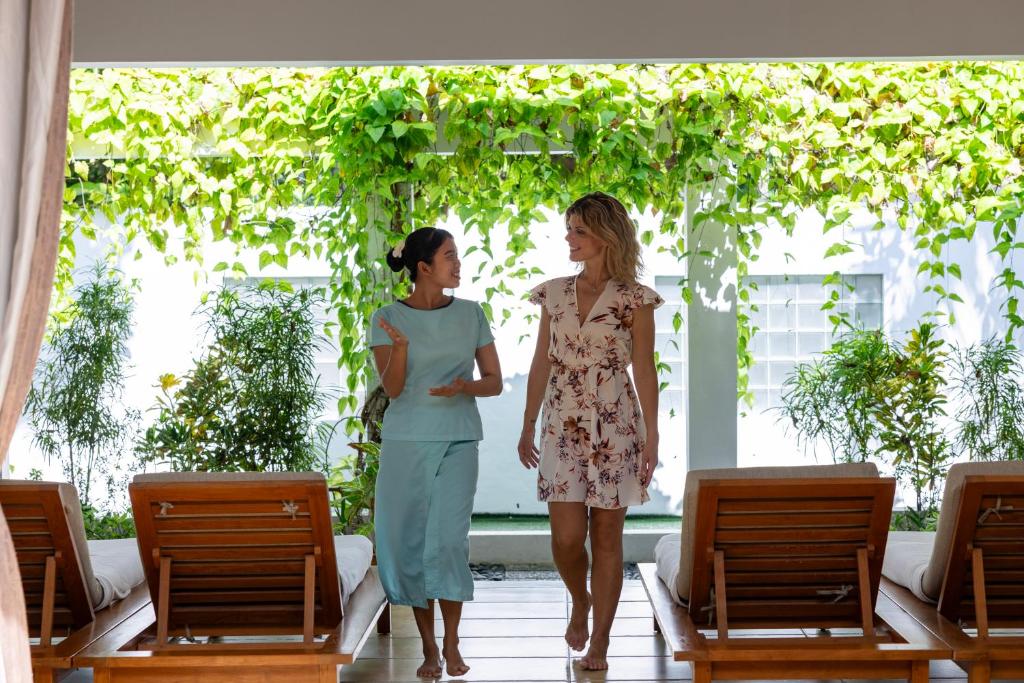 Divas sievietes sarunājas relaksējošā vidē ar zaļumiem un koka guļamvietām, radot mierīgu atmosfēru.