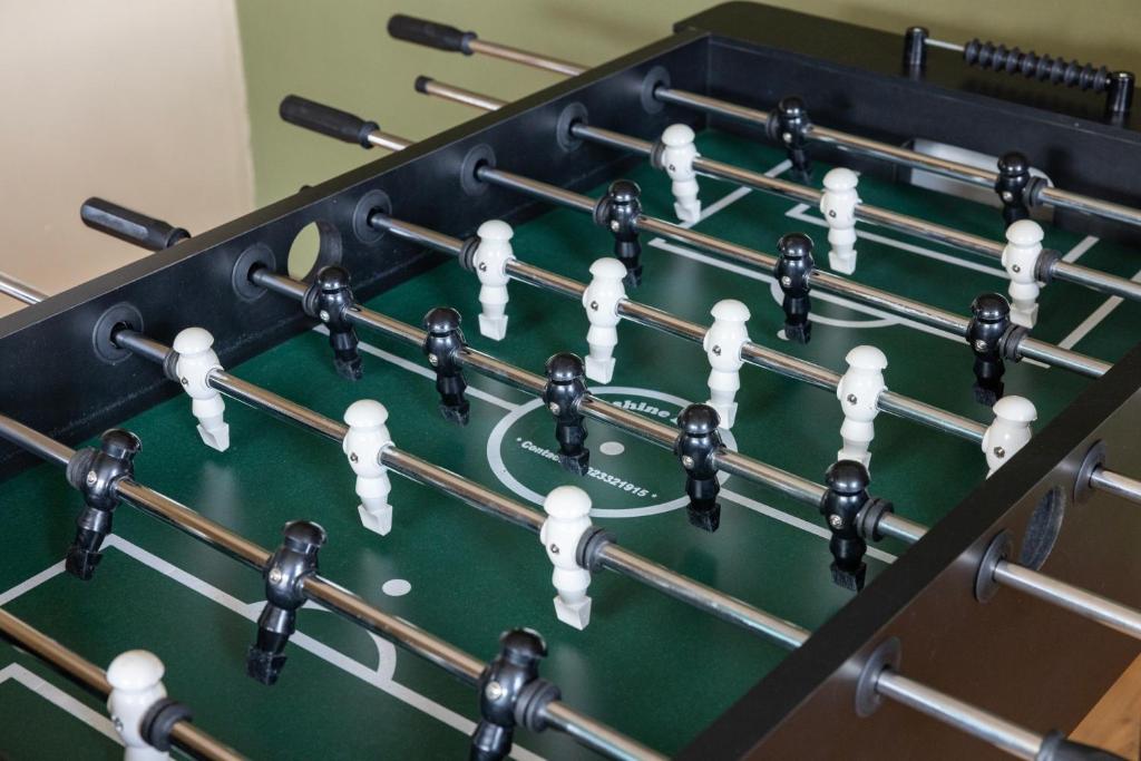 Galda futbols ar baltām un melnām figūrām, izvietotām uz zaļas spēles laukuma. Spēles piederumi un rokturi ir redzami.