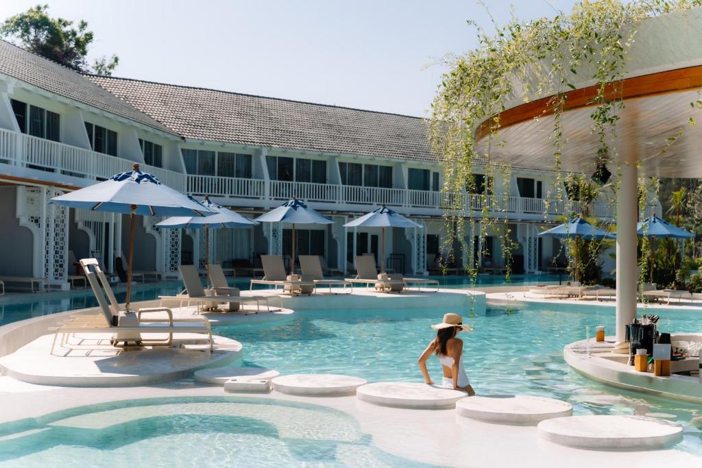 Lieliska atpūtas vieta pie baseina ar sauļošanās krēsliem un zilu saules aizsargu, kurā cilvēks relaksējas, baudot mierīgu atmosfēru.