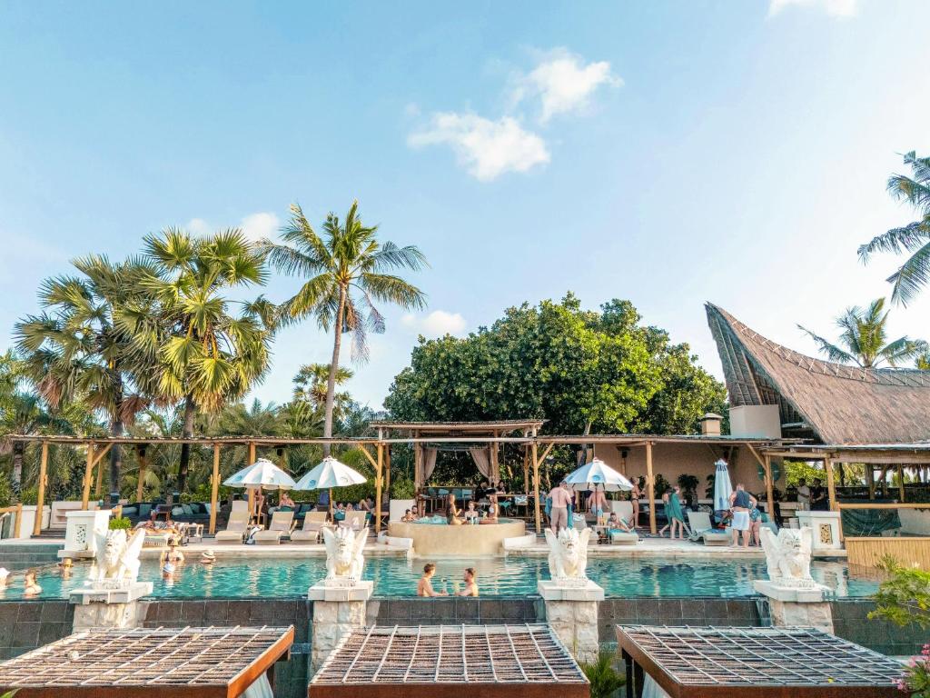 Tropu kūrorts ar peldbaseinu un palmām, kur cilvēki atpūšas un izbauda sauli. Eleganta arhitektūra un relaksējoša atmosfēra.