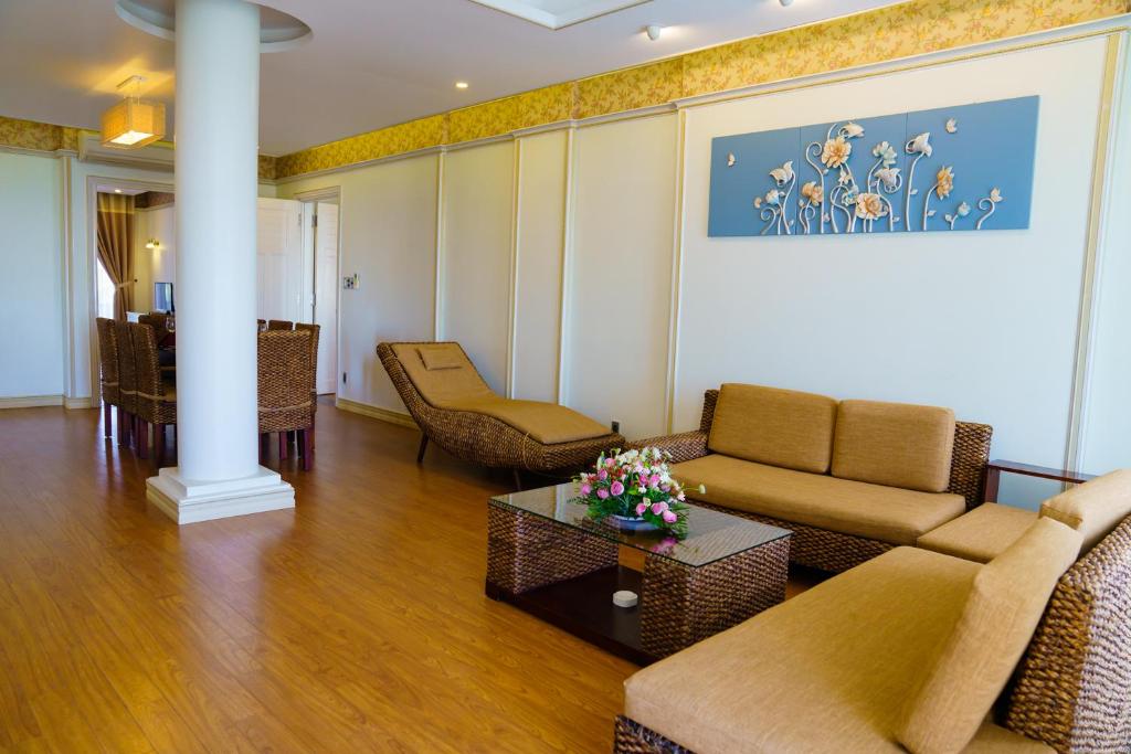 Gaiša un modernā viesistaba ar brūnu rotangpalmu mēbelēm un ziedu gleznu uz sienas, radot mājīgu atmosfēru. Telpā ir liels galds un eleganta atpūtas zona.