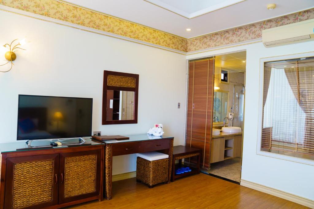 Mūsdienīgs viesnīcas numurs ar televizoru, rakstāmgaldu un piekļuvi vannas istabai caur stikla durvīm. Interjerā ir gaišas krāsas un dekoratīvi elementi.