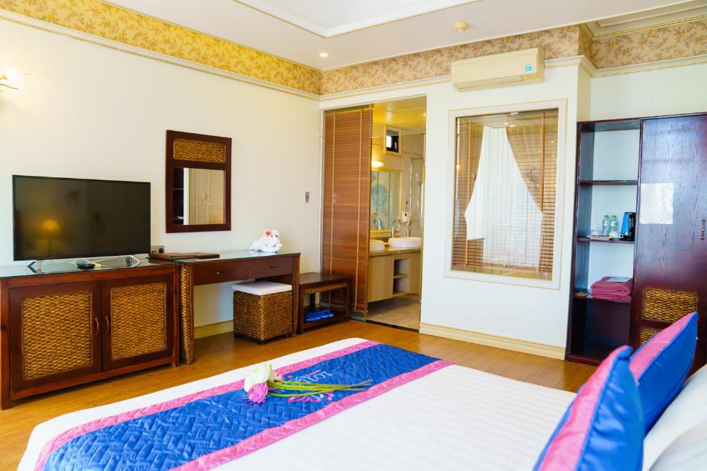 Mūsdienīga viesnīcu numura iekārtojums ar televizoru, vannas istabu un plauktiem. Gultā ir ziedi, un istaba ir gaiša un patīkama.