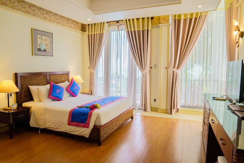 Mūsdienīgs viesnīcas numurs ar gultu, dekorētu ar spilveniem un gultas pārklāju, kas izceļas ar spilgtām krāsām. Logi ar aizkariem nodrošina dabisku apgaismojumu un skatu uz ārpusi.