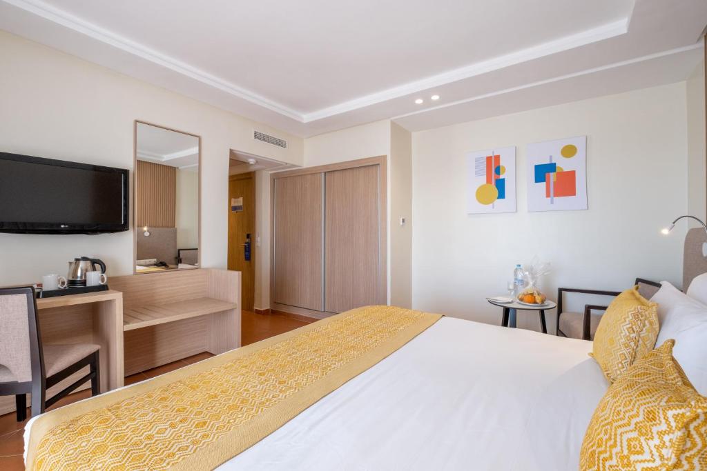 Mūsdienīgs viesnīcas numurs ar dzeltenu gultas pārklāju, televizoru, un mākslas darbiem uz sienas. Numurā ir arī rakstāmgalds un galdiņš ar augļiem un ūdeni.