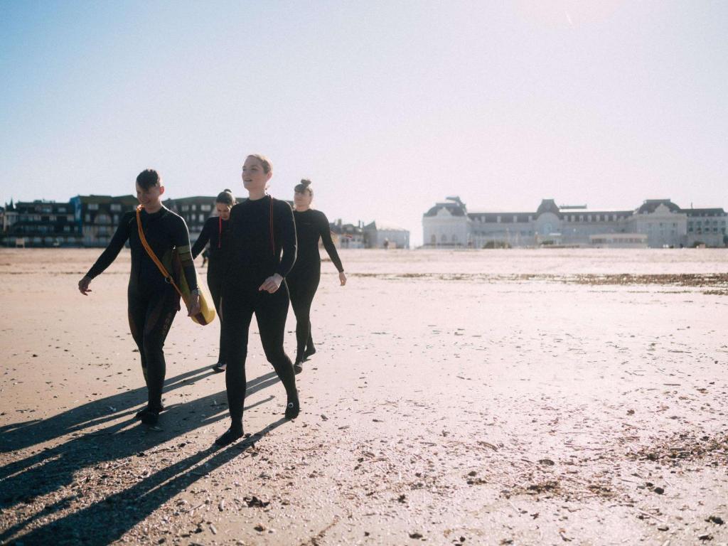 Grupa cilvēku, kas ģērbusies neoprēna tērpos, staigā pa pludmali pie Cures Marines Hotel Thalasso & Spa Trouville - MGallery Collection.