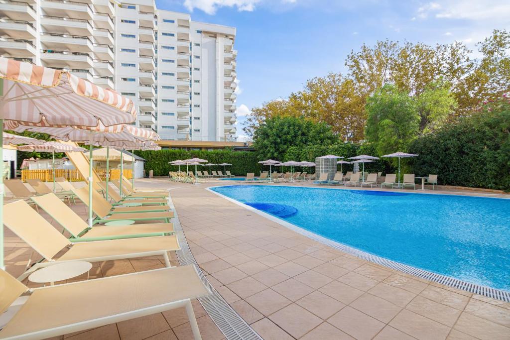 Baseins ar saules krēsliem un lietussargiem, apzaļumota teritorija un daudzdzīvokļu ēka fonā. Ideāla vieta relaksācijai un atpūtai.