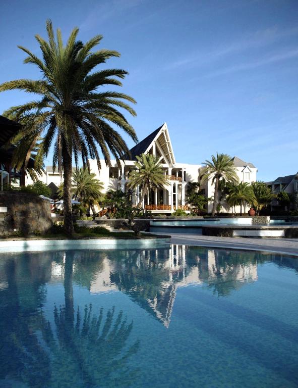 Tropu viesnīca ar baseinu un palmām, atspoguļojoties ūdenī, radot mierīgu un atpūtas atmosfēru.