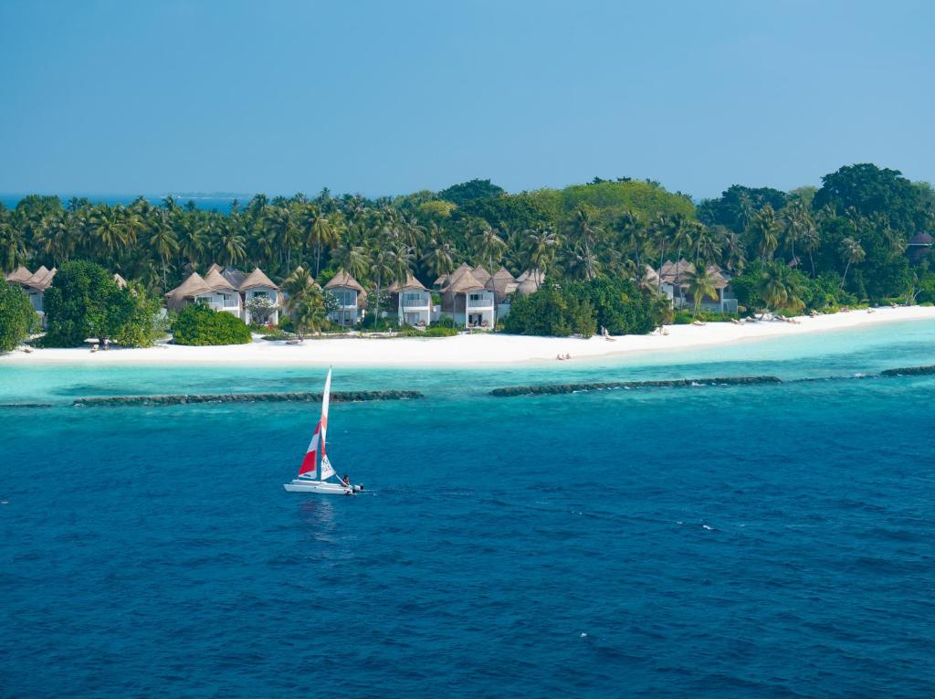 Skaista pludmale ar baltu smiltīm un palmām, kurā redzama jahta, kas burā pa kristāldzidru ūdeni, un luksusa viesnīcu komplekss fonā.