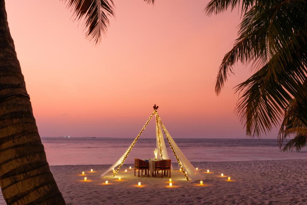 Romantisks pludmales iestatījums ar divām krēsliem un gaismiņām, apgaismots saulrieta fonā. Ideāla vieta romantiskai vakariņai pie jūras.