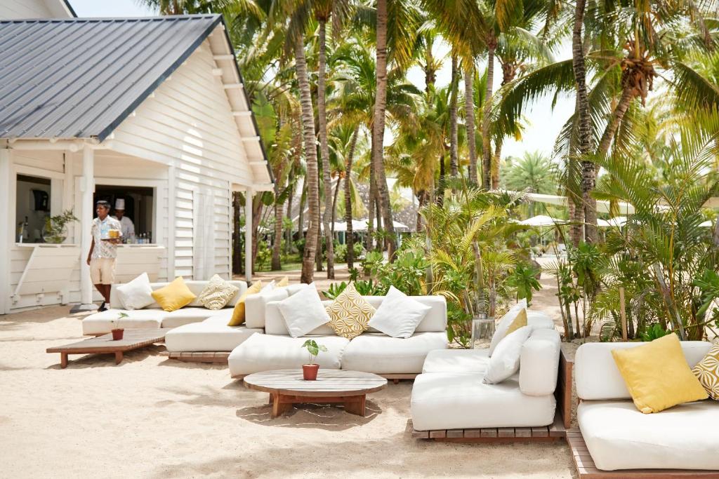 Pludmales kafijas stūrītis ar modernām dīvānu zonām, siltos toņos un palmu ainavu fonā. Ideāla vieta relaksācijai un baudīšanai.