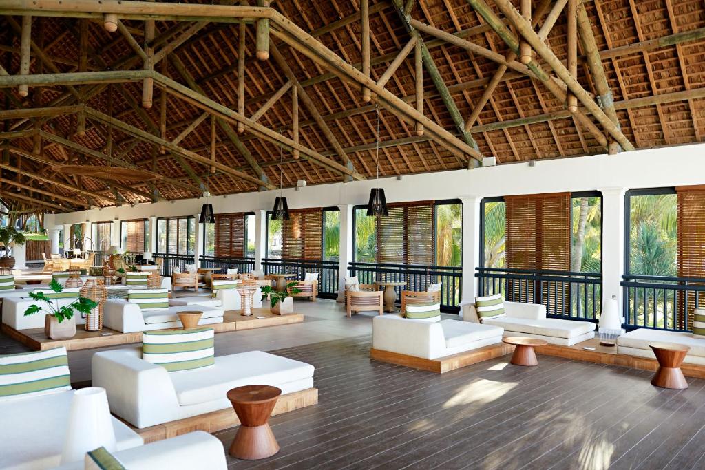 Mūsdienīgs un elegants atpūtas telpas interjers ar koka konstrukciju un plašiem logiem, kas nodrošina lielisku skatu uz dabu. Balti dīvāni ar zaļām spilveniem un koka galdiņi rada mierīgu atmosfēru.