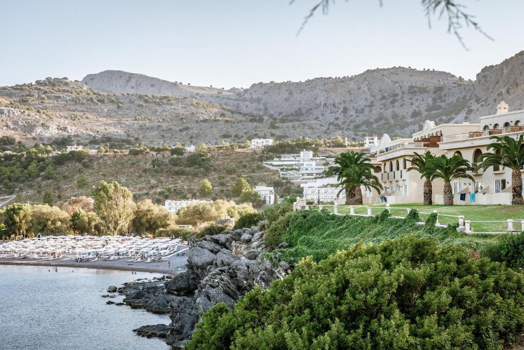 Klusas pludmales skats ar palmām un kalnainu ainavu fonā, kas ietver viesnīcas un laivu piestātni.