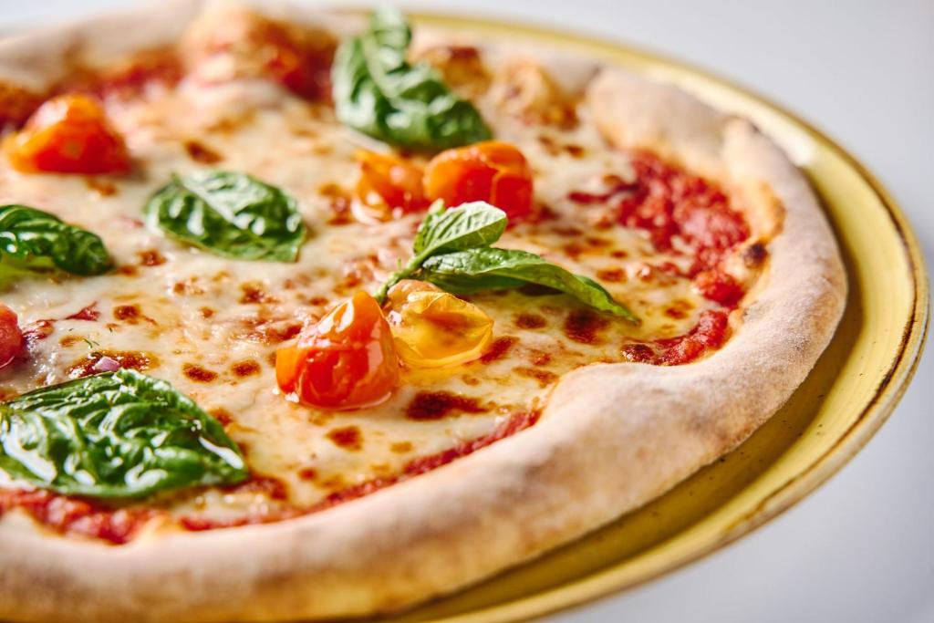 Svaigi cepta pica ar tomātiem un baziliku, pasniegta uz dzeltena šķīvja.