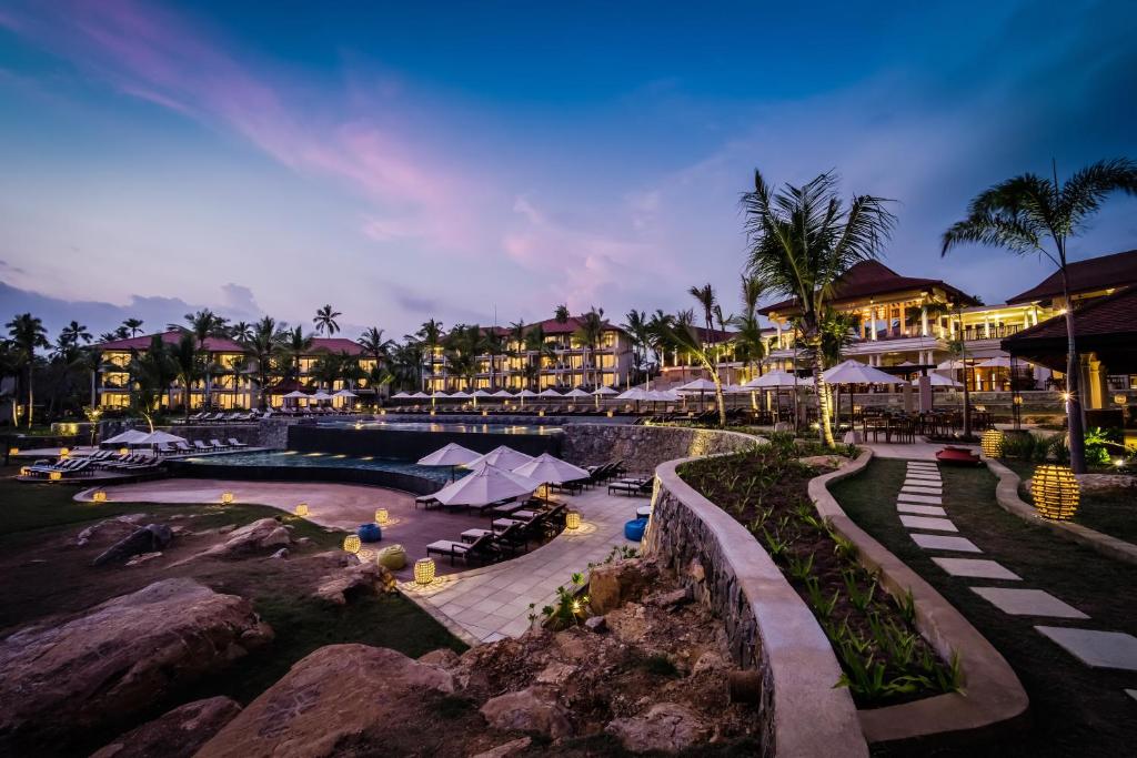 Elegants kūrorts ar baseinu un saules gultām, apvīts ar palmām un ziediem, romantiskā apgaismojumā krēslā. Ideāla vieta atpūtai un relaksācijai.