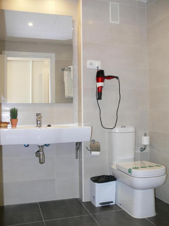 Mūsdienīgs vannas istabas interjers ar balto izlietni, spoguli un matu žāvētāju pie sienas. Vannas istabā ir arī tualete un atkritumu tvertne.