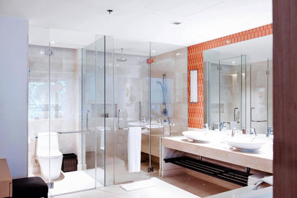Mūsdienīgs un elegants vannas istabas interjers ar stikla sienām, diviem izlietnēm un modernu dušu. Telpa ir gaiša ar minimālistisku dizainu un siltām krāsām.