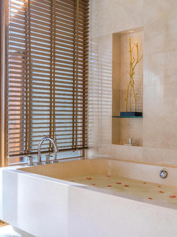 Mūsdienīga vannas istaba ar elegantu vannu, kurā peld ziedlapiņas, un stilīgām slēģu aizkariem. Interjers rada relaksējošu un komfortablu atmosfēru.