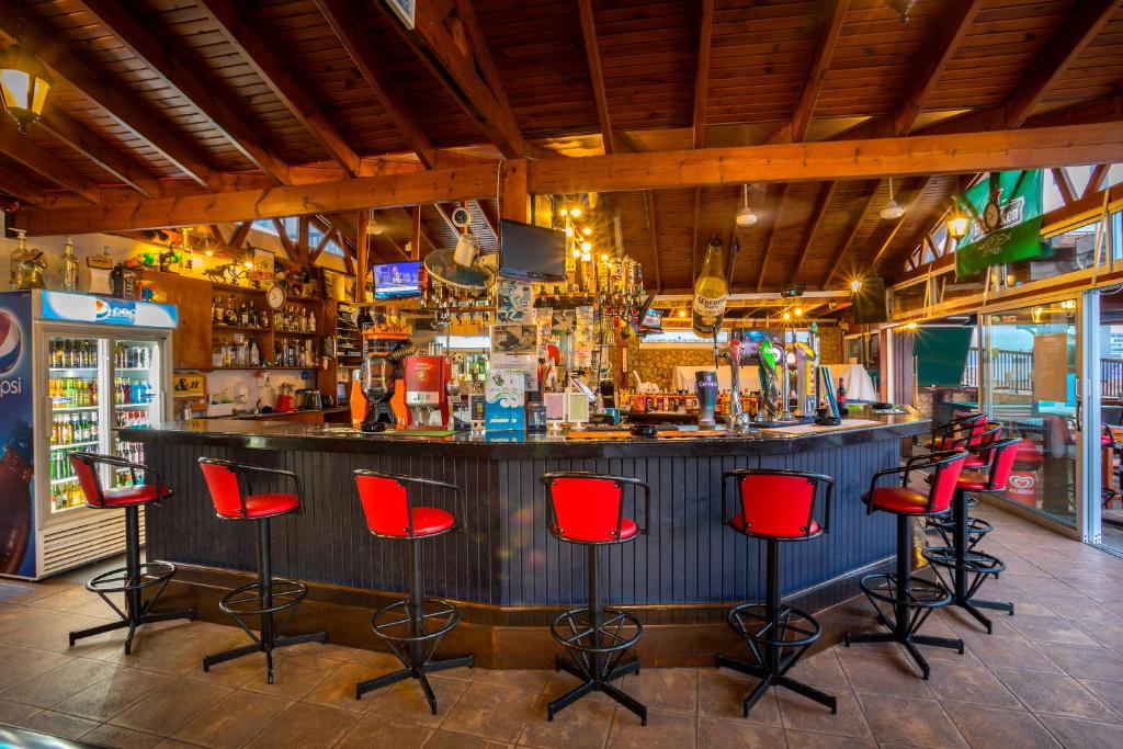 Skaists bārs ar koka interjeru un sarkaniem krēsliem, piedāvā plašu dzērienu izvēli. Gaisma rada siltu un viesmīlīgu atmosfēru.