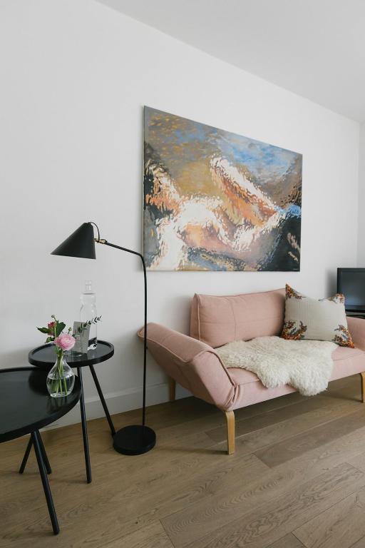 Mūsdienīgs viesistabas interjers ar rozā dīvānu, melnu lampu un mākslas darbu uz sienas, kas piešķir telpai eleganci un stilu.
