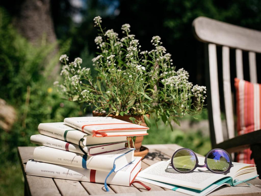 Dārzs ar grāmatām un saulesbrillēm uz galda, blakus puķu pods ar ziediem. Ideāla vieta relaksācijai un lasīšanai.