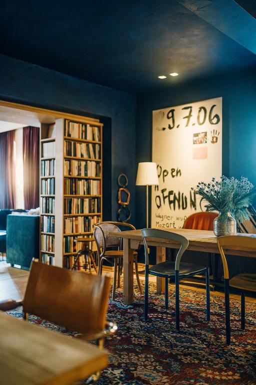 Mūsdienīgs un mājīgs interjers ar grāmatplauktu, koka galdiem un krēsliem, kā arī dekoratīvu vāzi ar ziediem uz galda. Sienā redzami mākslinieciski uzraksti un datums.