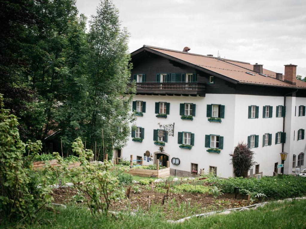 Vēsturiska ēka ar zaļām logu rāmēm, ieskauta kokiem un dārzu, radot mierīgu un idillisku atmosfēru.