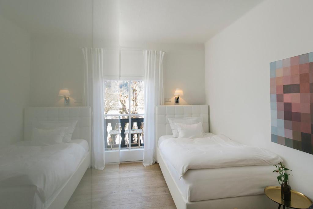 Mūsdienīgs divvietīgs guļamistabas interjers ar divām gultām, gaišām krāsām un logu, caur kuru redzama ainava. Sienā ir mākslas darbs, kas pievieno telpai modernu akcentu.