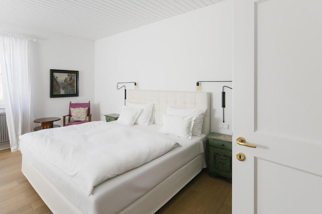 Mūsdienīga guļamistaba ar baltām sienām, lielu gultu un stilīgu interjeru, kurā ir koka grīda, krēsls un gaismas avoti. Guļamistaba rada mierīgu un relaksējošu atmosfēru.