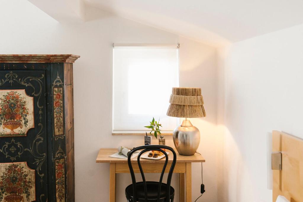 Mūsdienīga interjera telpa ar koka galdu, melnu krēslu un stilīgu lampu, blakus ir krāsains skapis un logs ar aizkariem.