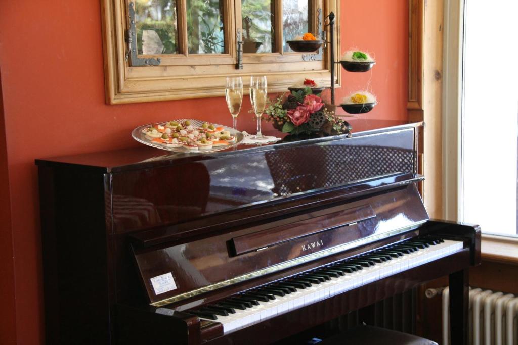 Uz klavierēm atrodas izsmalcināti uzkodas un šampanieša glāzes, radot elegantu atmosfēru. Sienas krāsa ir silta un mājīga, uzsverot interjera šarmu.