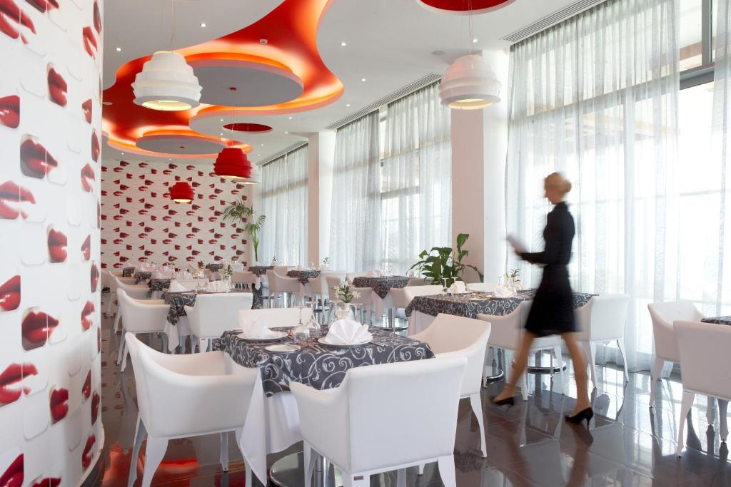 Mūsdienīgs restorāns ar elegantu interjeru, kurā ir baltas krēsli un galdi ar melnām galdautām, rotāti ar ziediem. Sienas dekorētas ar lūpu nospiedumiem, un telpā ir sarkani gaismas ķermeņi.