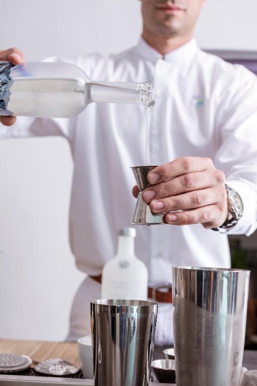 Bārmenis ielej dzērienu no pudeles mērtraukā, izmantojot stilīgu bārmeņa aprīkojumu. Attēls atspoguļo profesionālu bārmeņu darbu un kokteiļu pagatavošanu.