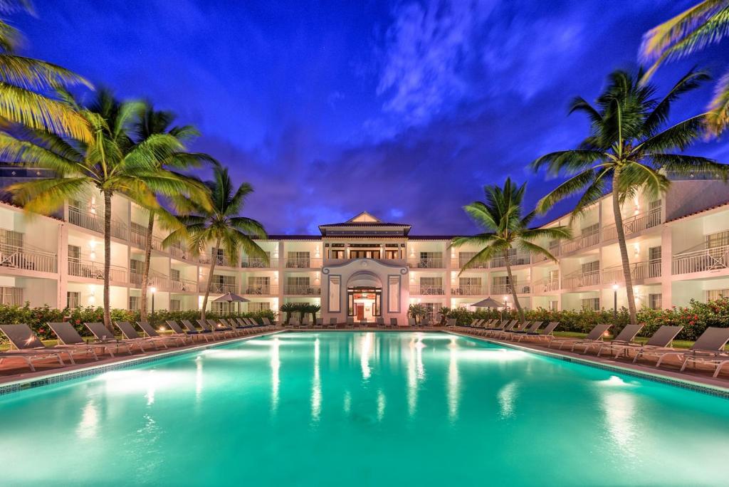 Luksusa viesnīca ar baseinu un palmām, kas atrodas tropiskā vidē, apgaismota vakara gaismā.