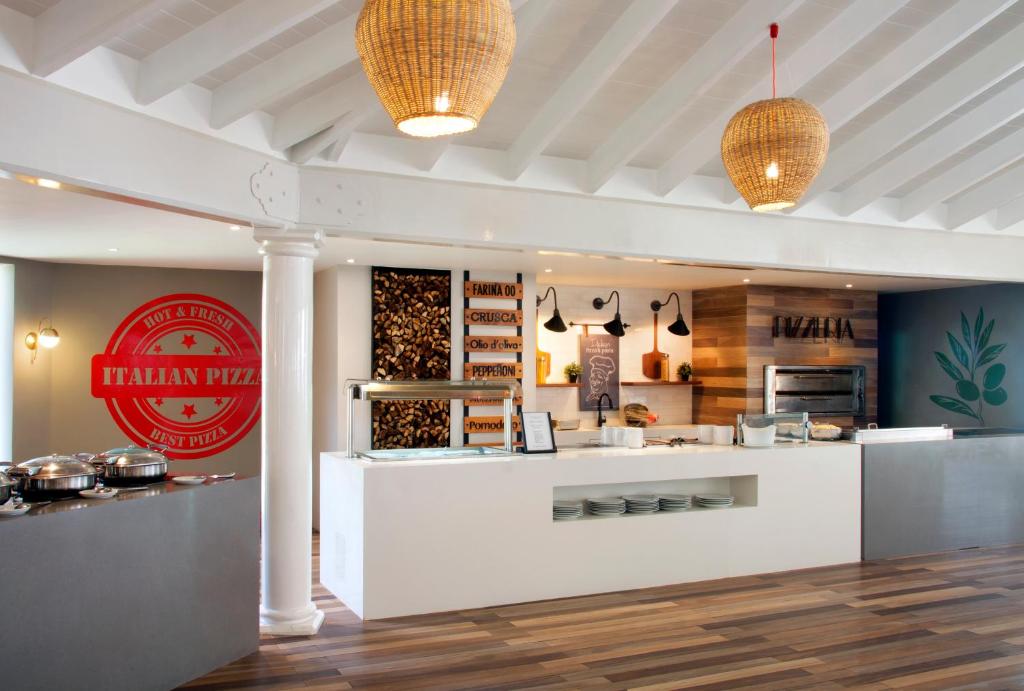 Mūsdienīga itāļu picērija ar siltām krāsām, koka akcentiem un kabeļu lampām, kas rada patīkamu atmosfēru. Redzams arī picērijas logo un dažādi picas sastāvdaļu izvietošanas risinājumi.