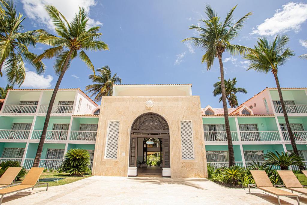 Viesnīcas ieeja ar palmām un krāsainām ēkām, kas rada tropisku atmosfēru. Ideāla vieta atpūtai un relaksācijai.