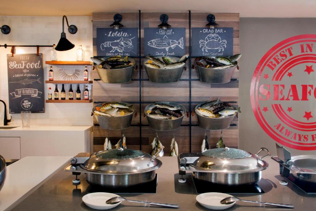 Restorāna jūras velšu stends ar svaigu zivi un krabjiem, kas izkārtoti metāla traukos, pie sienas ir ēdienkarte. Redzami arī dažādi dzērieni un šķīvji.