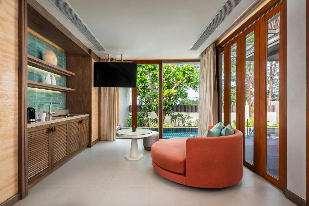 Mūsdienīgs viesnīcas numurs ar ērtiem mēbelēšanas elementiem, tostarp apaļu rozā dīvānu un skatu uz dārzu caur lieliem logiem. Interjers ir gaišs un elegants, radot relaksējošu atmosfēru.