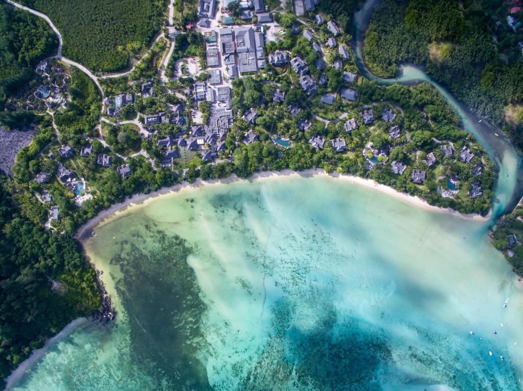 Aerial view of a tropical resort nestled along a sandy beach, surrounded by lush greenery and clear turquoise waters.