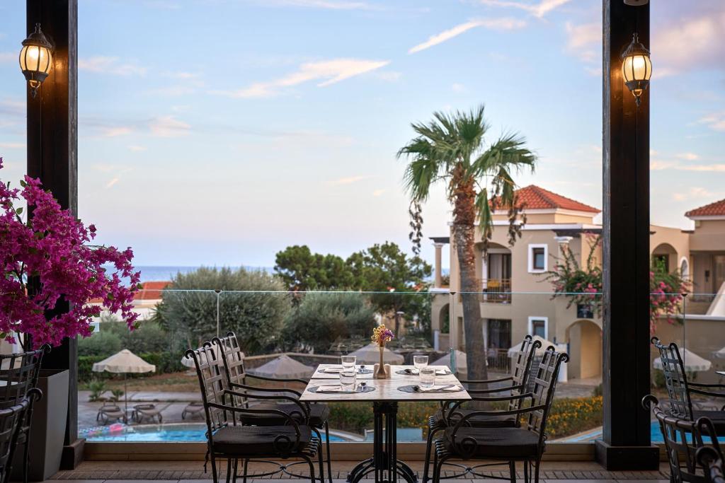 Elegants restorāns ar brīnišķīgu skatu uz jūru, kurā redzami galdi un rozā ziedi. Apkārt esošā daba un arhitektūra rada relaksējošu atmosfēru.