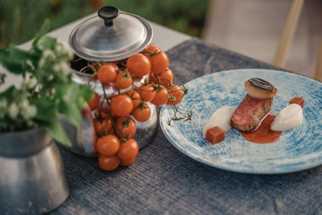 Grezni ēdieni uz zila šķīvja, apvienojot gaļu un garnējumu, ar ķiršu tomātiem un zaļumiem blakus. Ideāla atmosfēra gastronomiskai pieredzei.