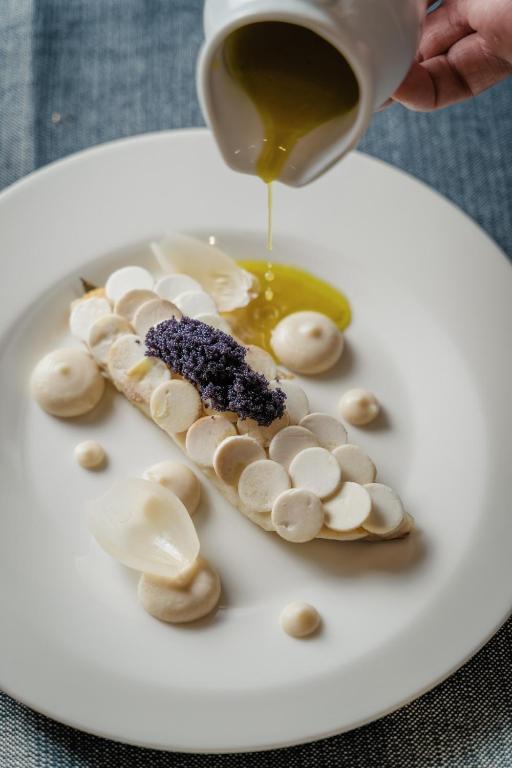Elegant dish featuring a layered presentation of circular garnishes, accompanied by delicate purées and a drizzle of olive oil. The composition is enhanced with edible flowers, creating a visually striking culinary experience.