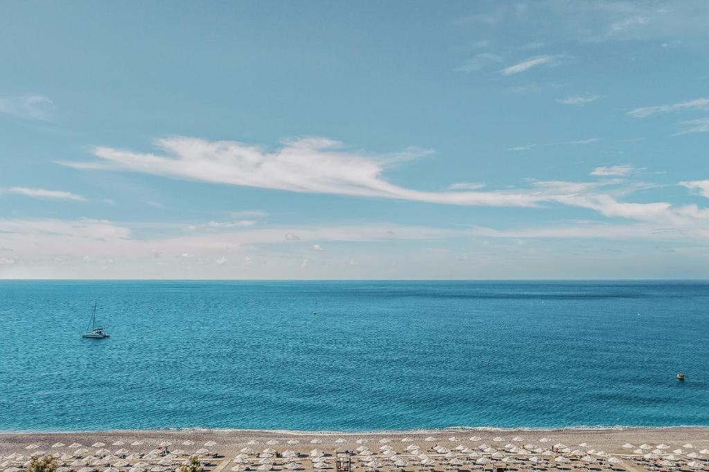 Zilā jūra un skaidrs debesis ar dažām mākonēm, laivu peldēšana un pludmale ar saulessargiem.