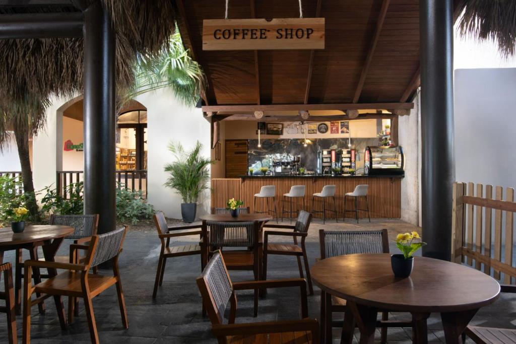 Kafejnīca ar koka mēbelēm un mājīgu atmosfēru, kurā redzami plāni galdi un krēsli, kā arī kafejnīcas bārs ar dzērienu automātiem un vitrīnu.