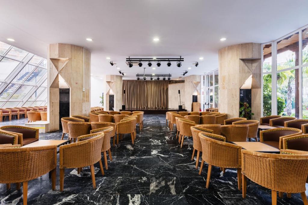 Moderns pasākumu zāles interjers ar krēslu rindām un skatuvi. Plašs logu apgaismojums un eleganta grīda rada patīkamu atmosfēru.