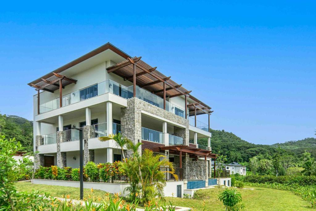 Mūsdienīga trīsstāvu villa ar stikla balkoniem un akmens fasādi, ieskauta zaļā ainavā un kalnu fonā. Ideāla izvēle atpūtai vai dzīvošanai.